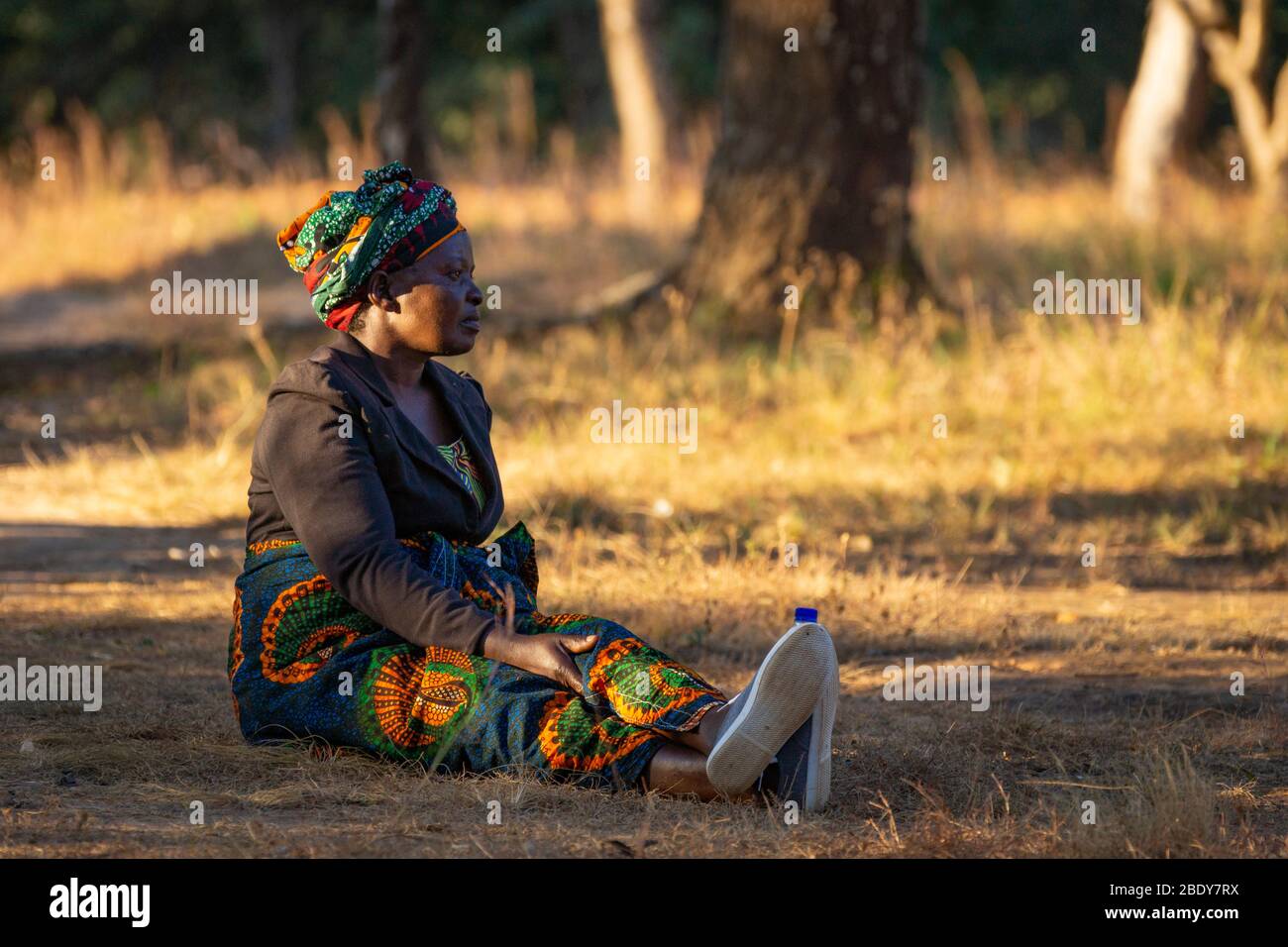 Die malawische Frau in farbenfrohen Kleidern sitzt am frühen Abend am Straßenrand Stockfoto