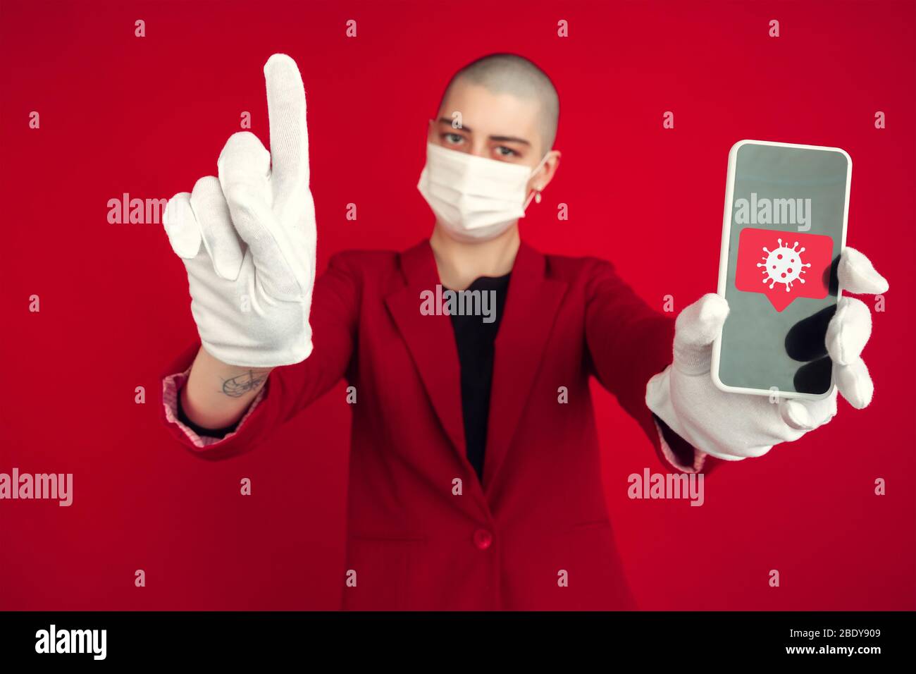 Frau auf rotem Hintergrund trägt Gesichtsmaske, zeigt Telefon mit Coronavirus-Illustration. Konzept der Verbreitung, Schutz, Prävention, weltweiten Epidemie und Pandemie des Coronavirus. Quarantäne, Isolierung. Stockfoto