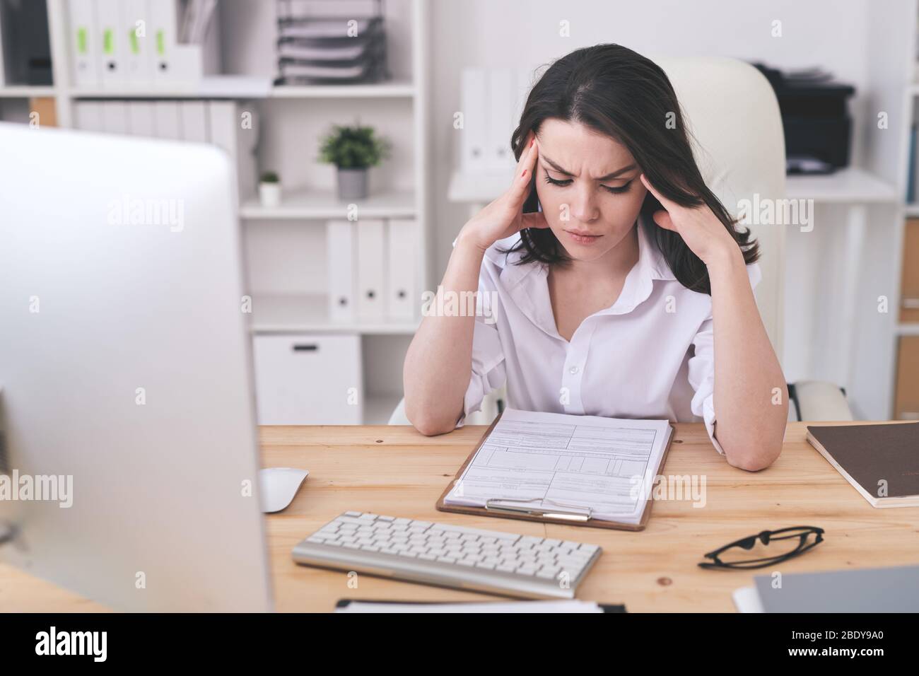Junge ernsthafte Geschäftsfrau konzentriert sich auf das Lernen von Finanzdokumenten, während sie am Tisch sitzt und sich über Papiere beugt Stockfoto