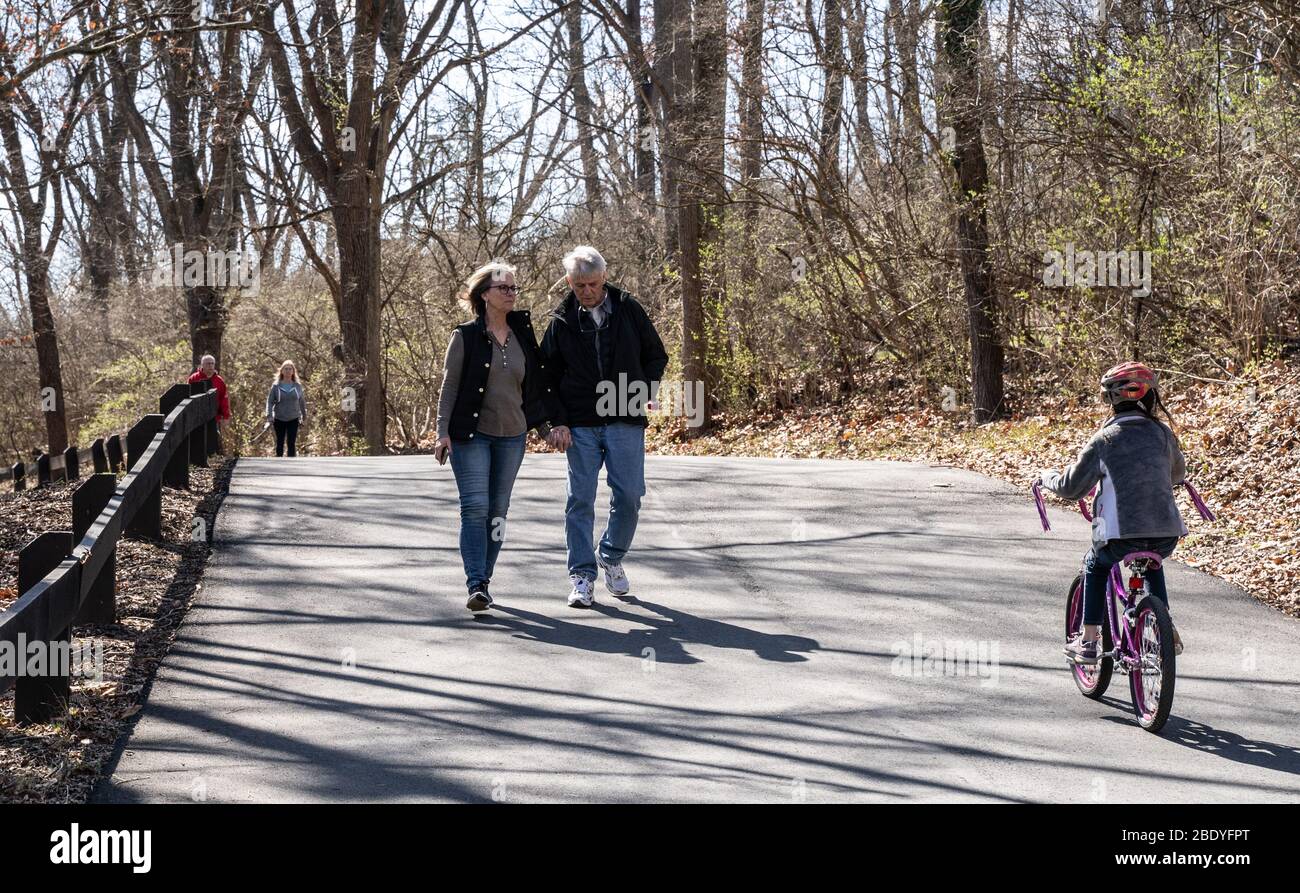 Berks County, Pennsylvania, USA-15. März 2020: Ältere Paare gehen mit Händen, während ein junger Fahrradfahrer vorbeifährt. Leute wurden gebeten, soziale dist Stockfoto