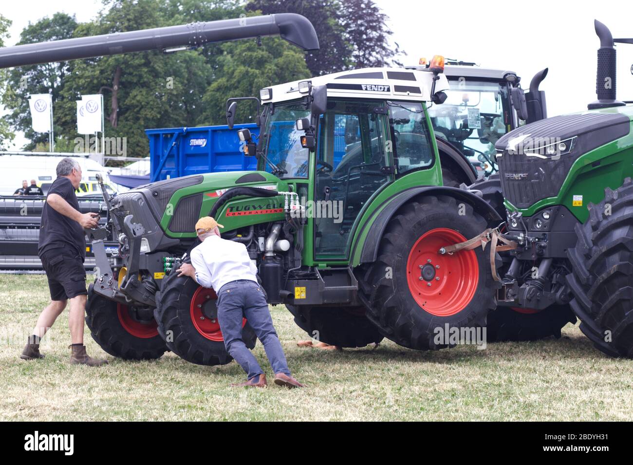 Männer schieben einen Fendt Traktor an seinen Platz, der an einem anderen Fendt Traktor befestigt ist. Stockfoto