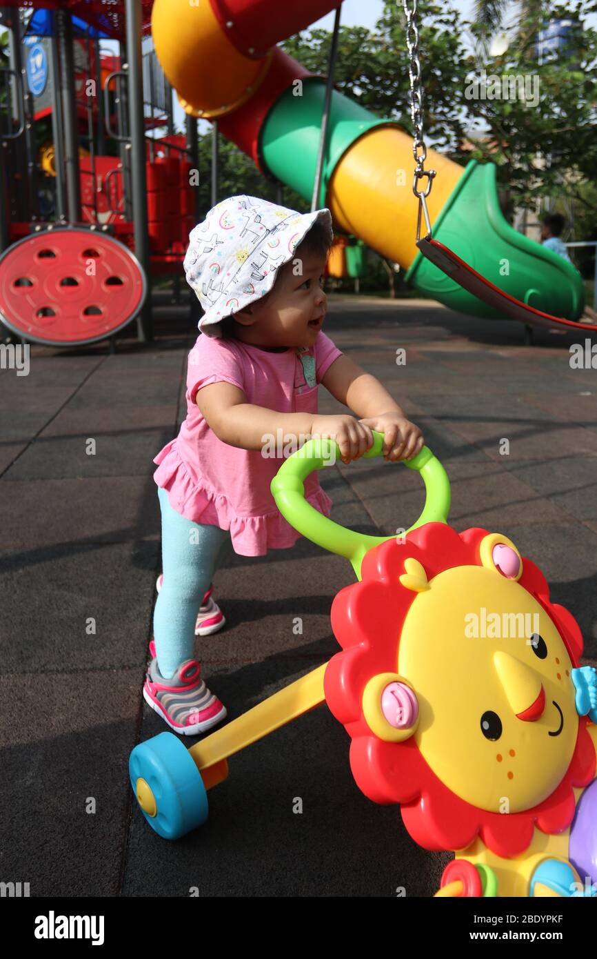 1 Jahr altes Mädchen, Kleinkind, Gesicht asiatischen Baby, spielen in der Stadt Spielplatz spielen Park, öffentlichen Raum mit ihrem Baby Push Walker Stockfoto