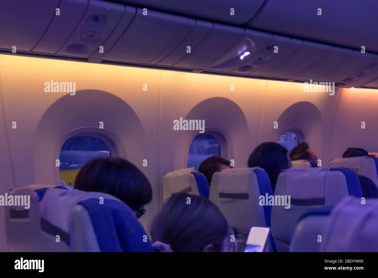 Flugzeugkabine mit Passagieren in Stühlen während eines Abendfluges. Reihe von Ebenen Sitzen am Fenster. Weicher Fokus und verschwommenes Foto Stockfoto