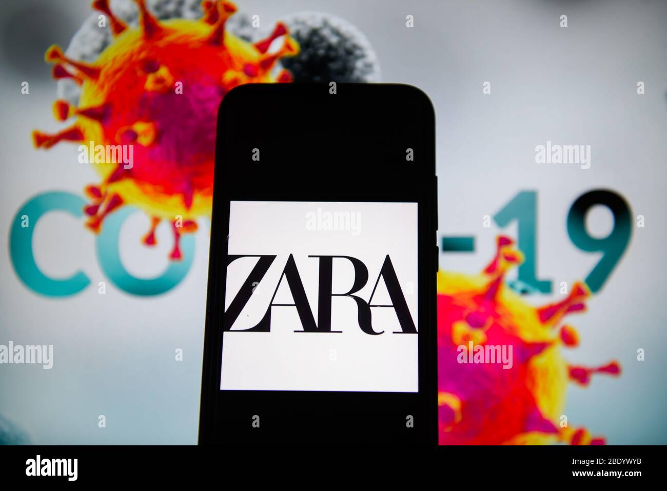 In dieser Abbildung ist ein Zara-Logo auf einem Smartphone mit einem COVID 19-Muster im Hintergrund zu sehen. Stockfoto