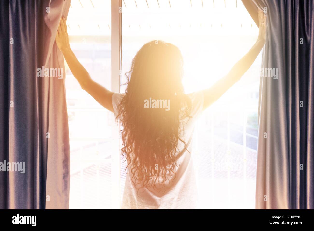 Frau öffnet die Vorhänge am Morgen im Schlafzimmer. Sonnenlicht scheint in den Raum. Konzept des neuen Tages beginnt. Verschwommenes Foto mit weichem Fokus. Stockfoto