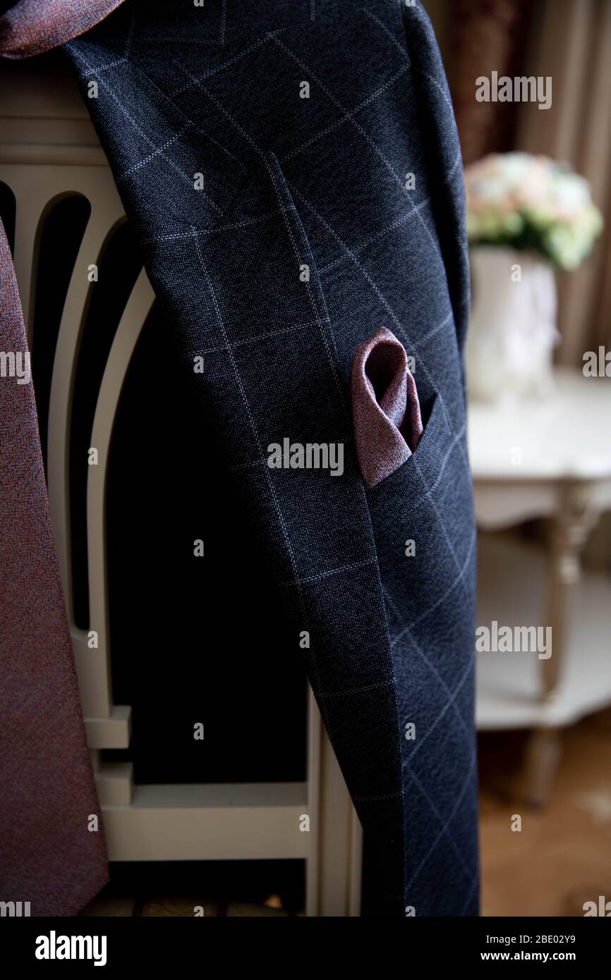 Auf der Rückseite eines Stuhls hängt der Hochzeitsanzug eines Mannes mit Boutonniere. Stockfoto