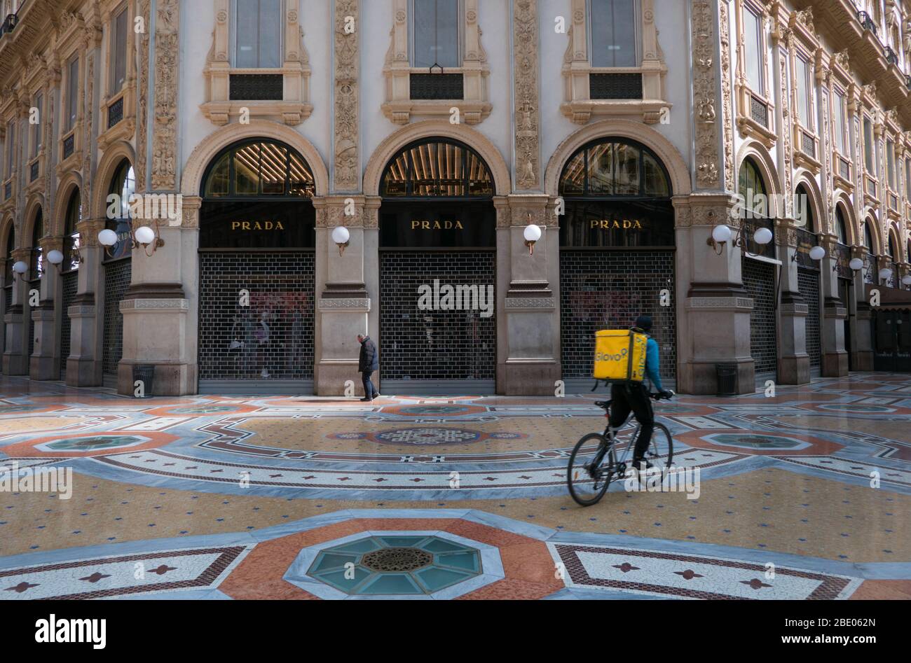 Leeres Wahrzeichen und Denkmal: Galleria Vittorio Emanuele II in Mailand, Italien während des Notfalls COVID-19. Obdachloser Mann und Fahrradfahrer in der Nähe von Prada Geschäft Stockfoto