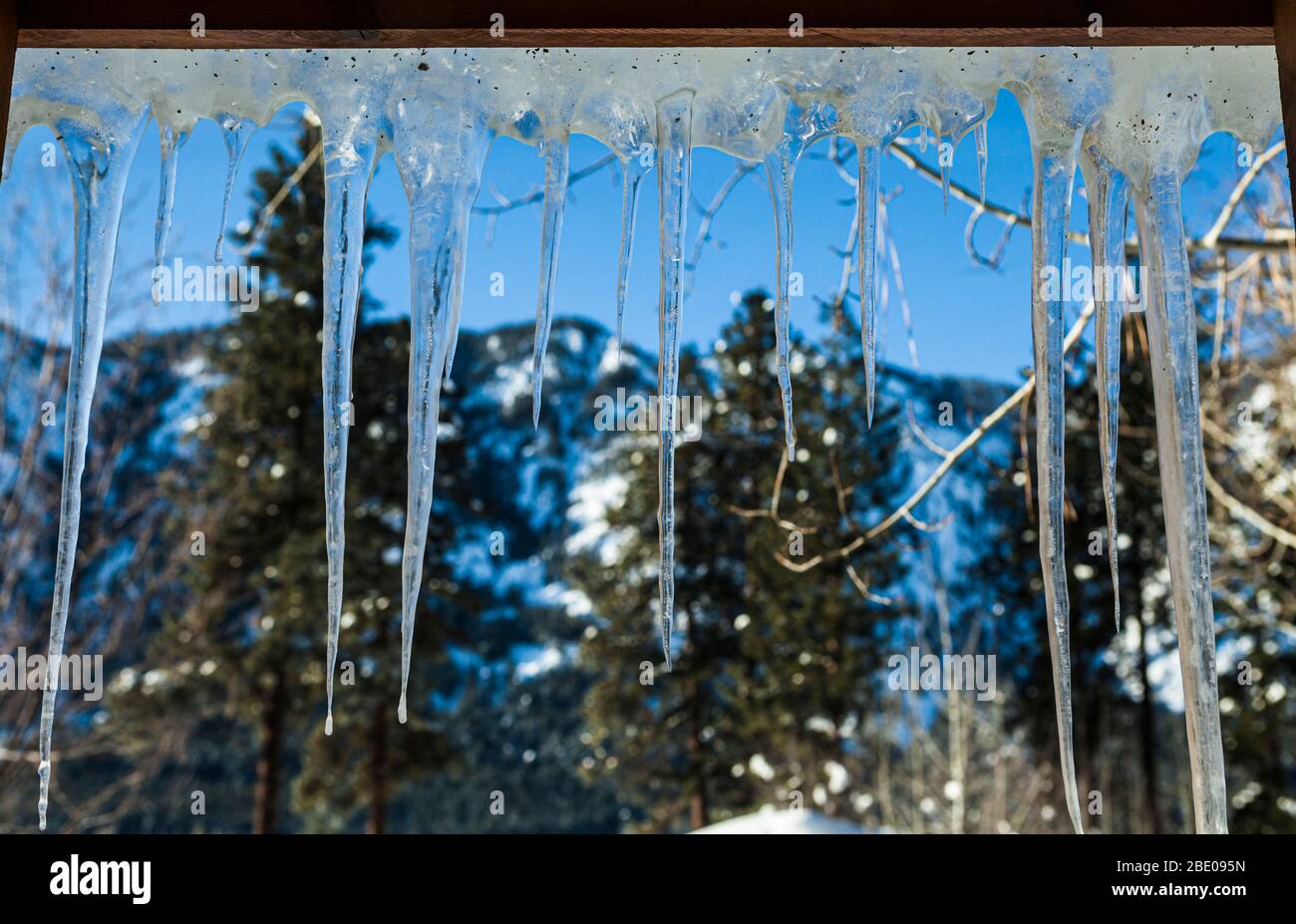 Eiszapfen hängen vom Dach und sehen von innen ein Fenster mit Blick nach draußen. Stockfoto