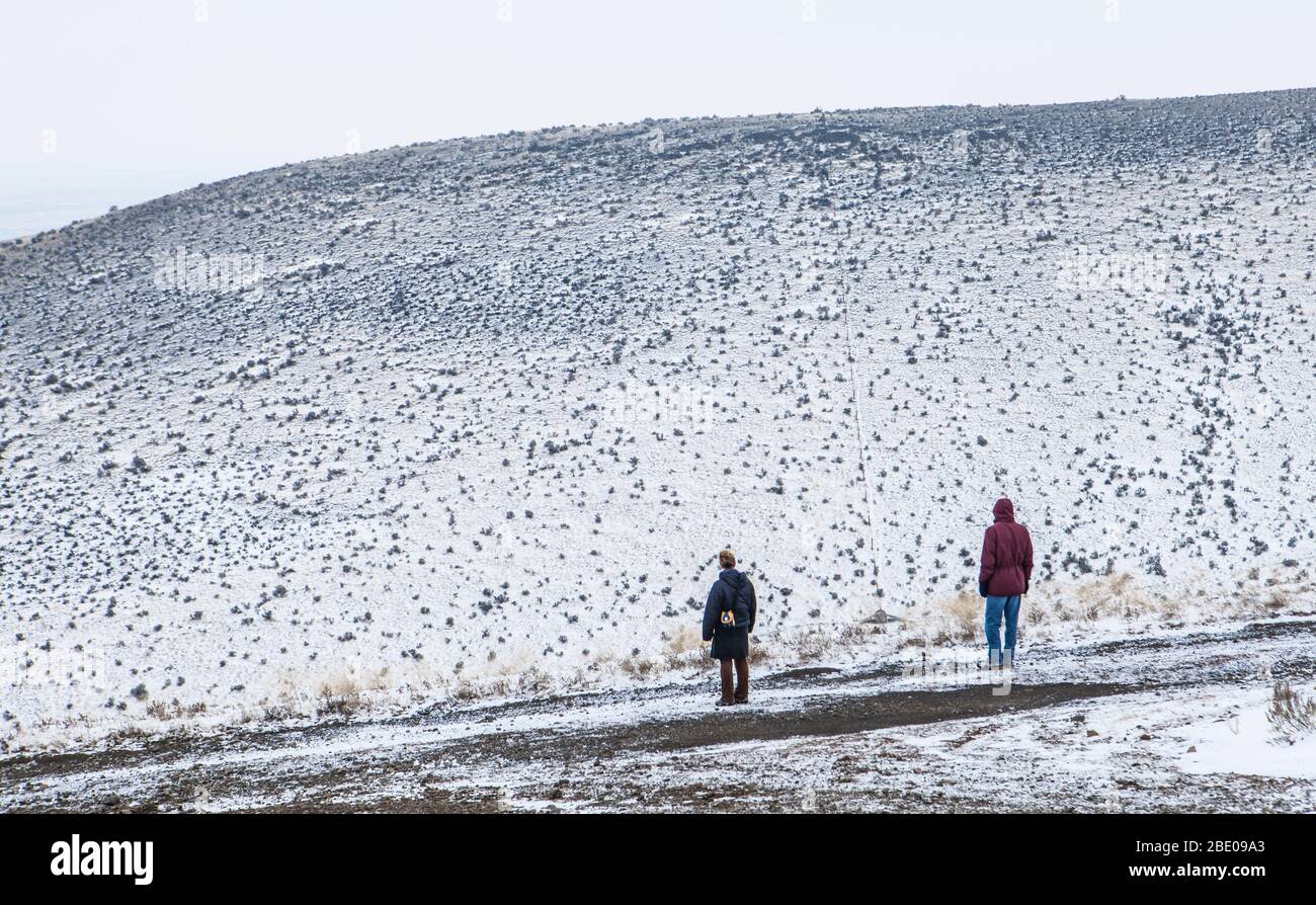 Ein Mann und eine Frau stehen auf einer Straße mit Blick auf einen schneebedeckten Hügel in den beezley Hügeln außerhalb von Ephrata, Washington, USA. Stockfoto