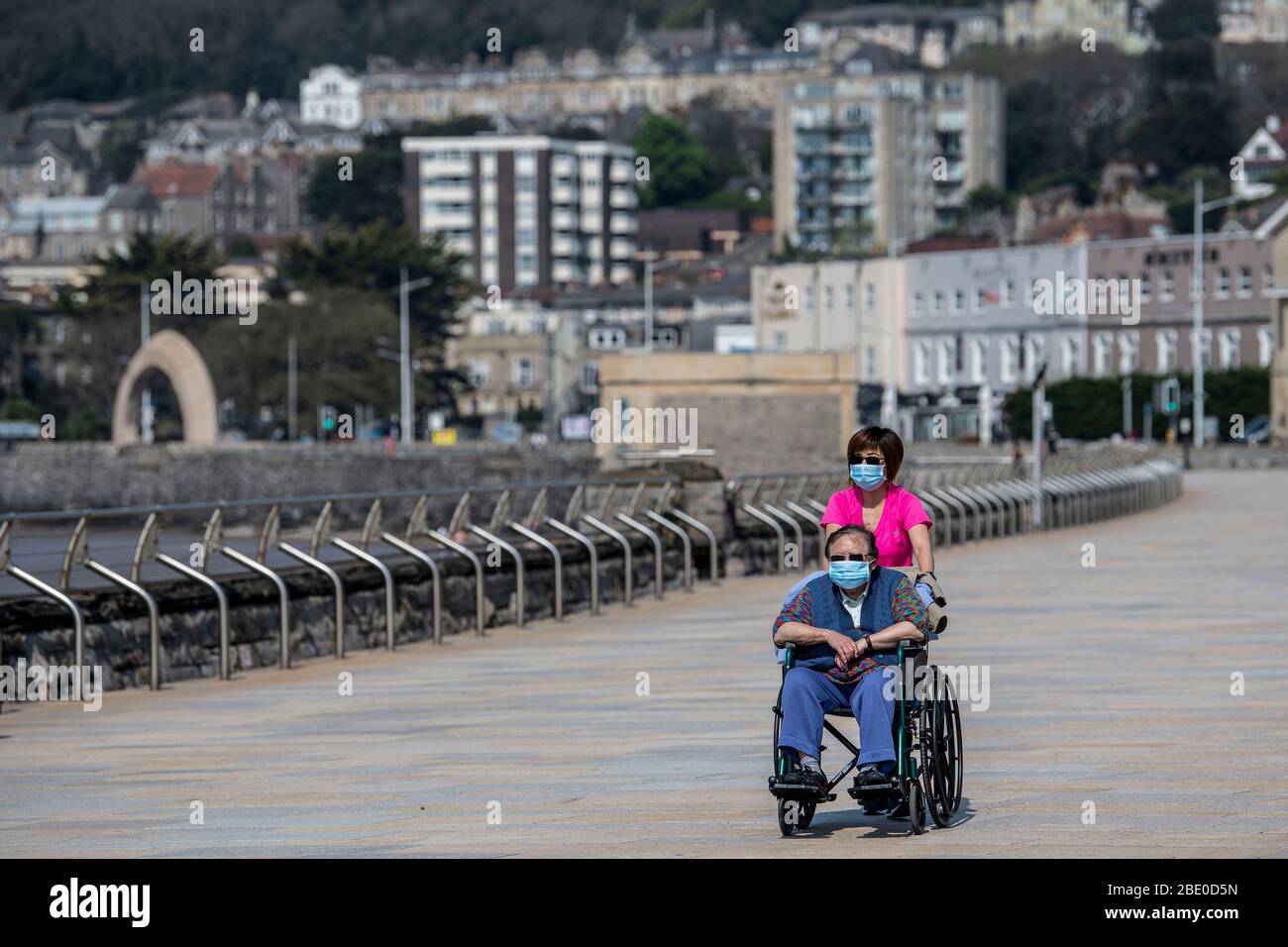 Eine Frau, die während der Sperrung der Coronavirus-Pandemie einen Mann im Rollstuhl posiert, beide mit Schutzmaske auf der Marine Parade in Weston-super-Mare. Stockfoto