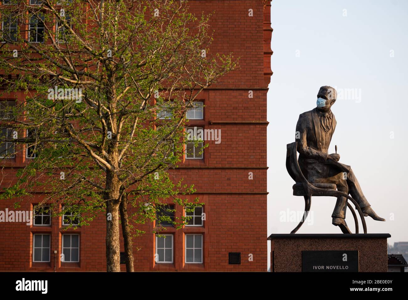 Die Ivor Novello Statue in Cardiff Bay, Wales, UK, trägt eine blaue chirurgische Gesichtsmaske während des Coronavirus (COVID-19) Lockdown. Stockfoto