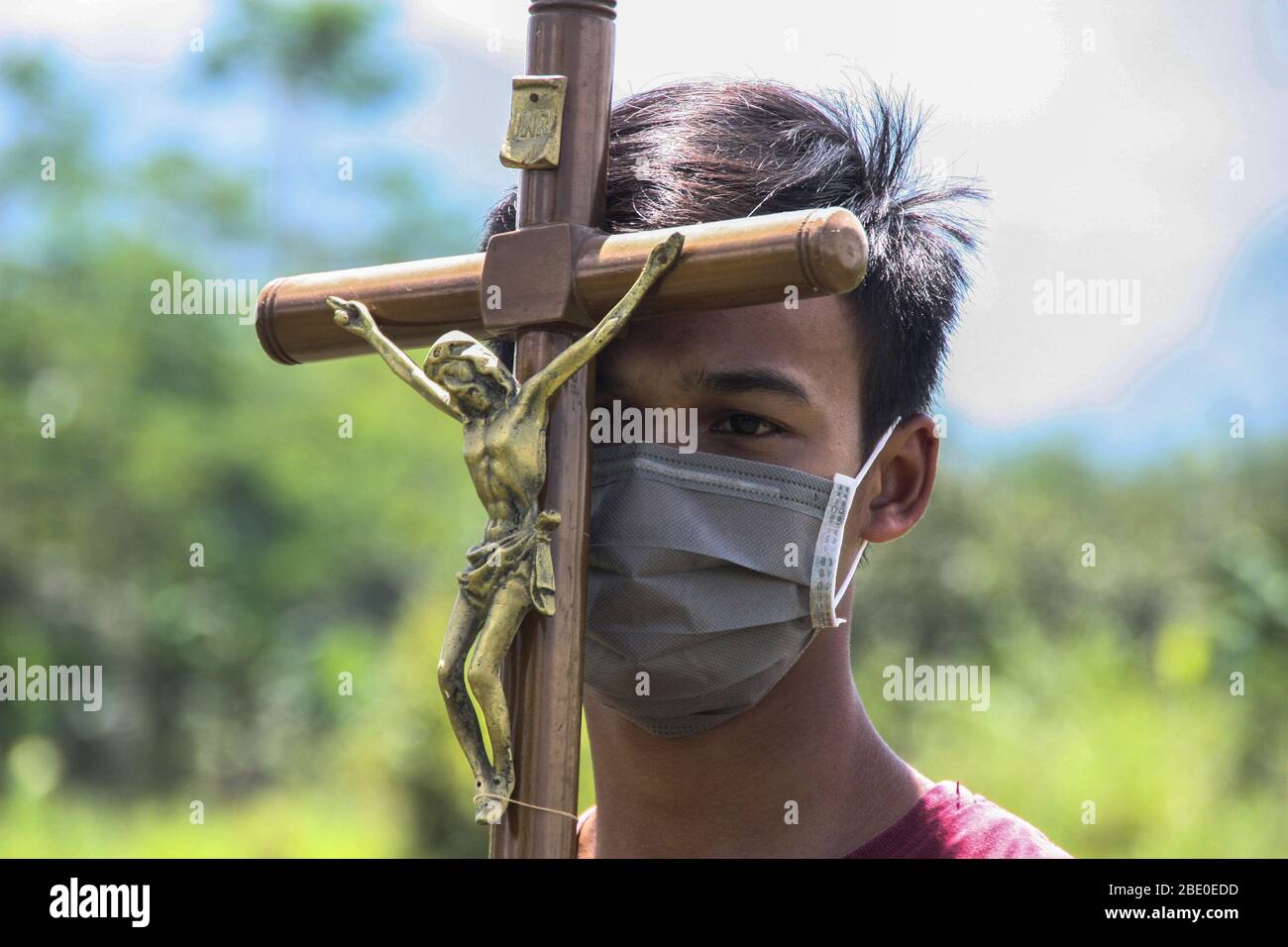 Sleman, Yogyakarta, Indonesien. April 2020. Ein katholischer junger Mann trägt eine Maske und hält das Kreuz Jesu vor dem Hintergrund des Merapi-Berges, während er den Weg zum stillen Kreuz von Karfreitag vier jungen Katholiken führt. Ostern und andere Gottesdienste für Christen und Katholiken auf der ganzen Welt 2020 unterbrochen durch den Ausbruch des Corona oder Covid-19 Virus. Kredit: Slamet Riyadi/ZUMA Wire/Alamy Live News Stockfoto