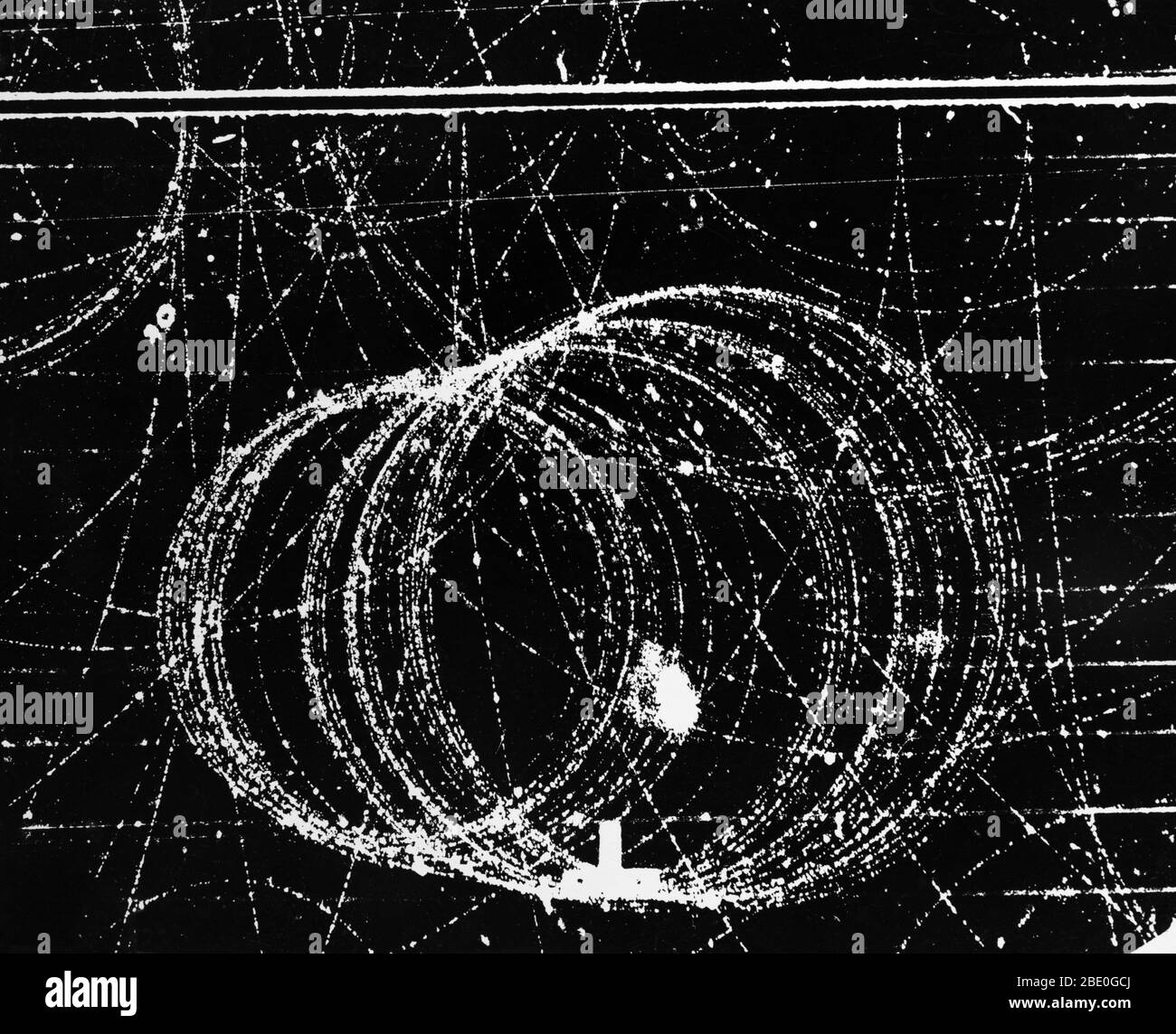 Kreisförmige Spur von 42 Meu Positron in 12,000 Gauß Magnetfeld. Die Weglänge der Positronenbahn auf diesem Foto beträgt fast 8 Meter. Elektronen- und Positronenspiralbahnen in einer Wolkenkammer im Lawrence Berkeley Laboratory, Kalifornien. Elektron und Positron begannen ihr Leben am unteren Rand des Rahmens; sie wurden durch einen von rechts eintretenden Gammastrahl erzeugt. Das Positron, ein Elektron mit positiver Ladung, spiraliert (größere Schleifen) in die linke untere Ecke, während sich die kleineren Schleifen des Elektrons nach oben bewegen. Die anderen Spuren, die den Rahmen überqueren, sind ebenfalls darauf zurückzuführen Stockfoto