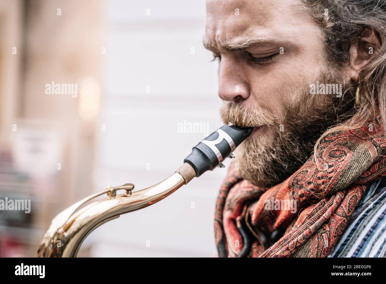 Gesicht eines Saxophonisten mit langen Haaren und Bart in Hippiekleidung, der mitten auf der Straße spielt Stockfoto