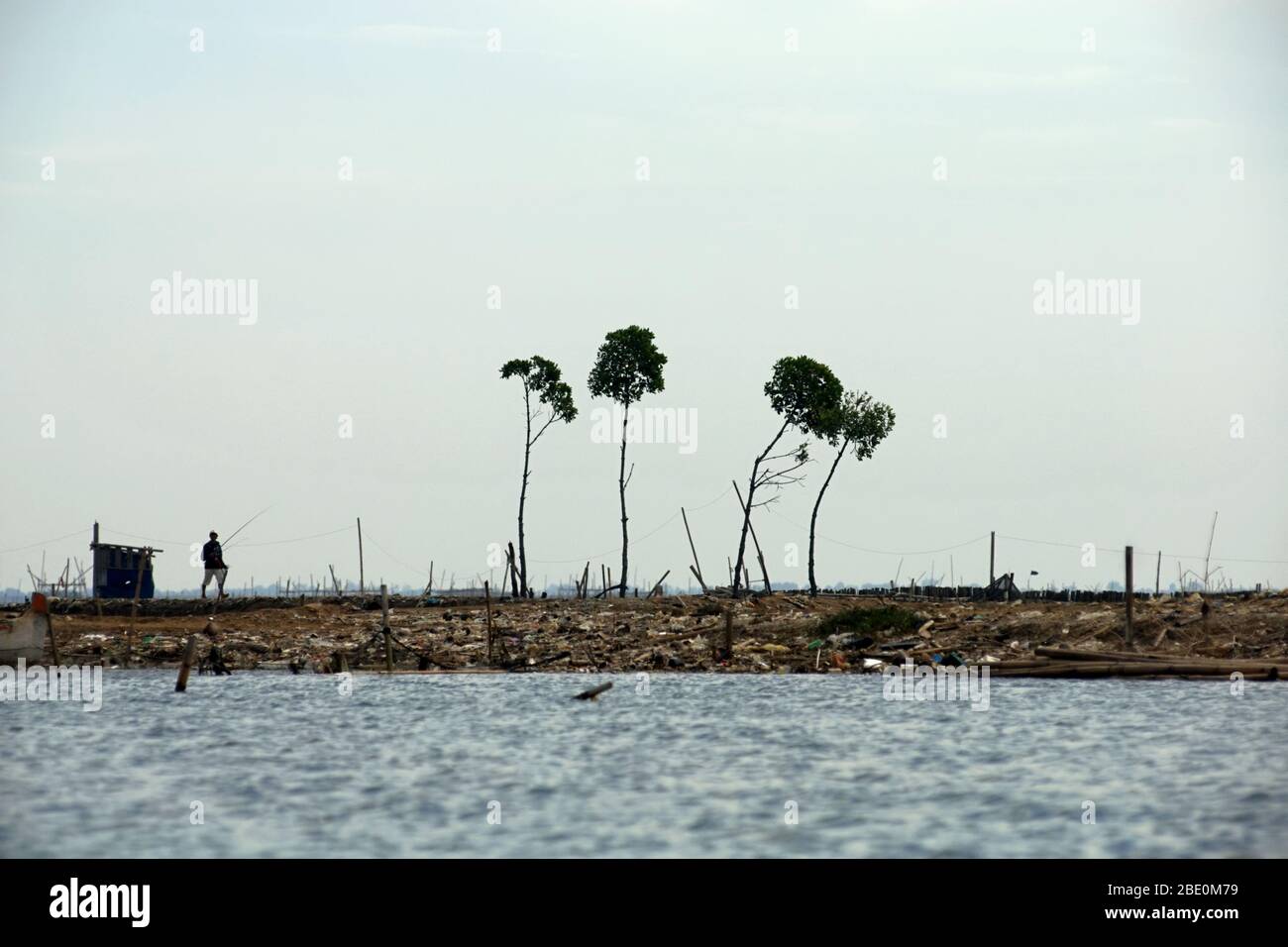 Ein Fischer, der auf einem zurückgewonnenen Land an der Mündung des Flutkanals von Jakarta, an der Provinzgrenze zwischen West-Java und Jakarta, Indonesien, spazierengeht. Stockfoto