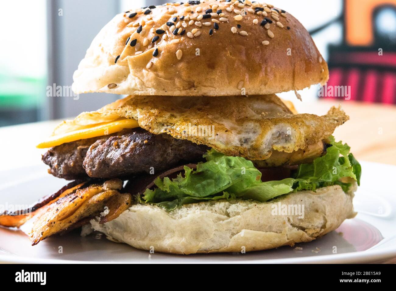 Großer Hamburger mit Ei, Banane, Käse und Fleisch auf einem weißen Teller. Stockfoto