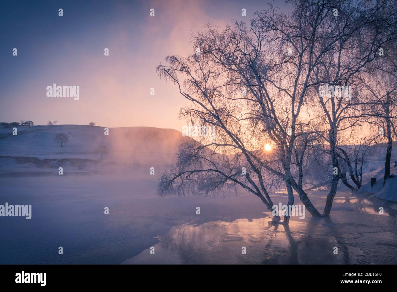Winteraufgangszeit über gefrorenem Fluss und Reim von mattierten Bäumen an einem sehr kalten Morgen. Stockfoto