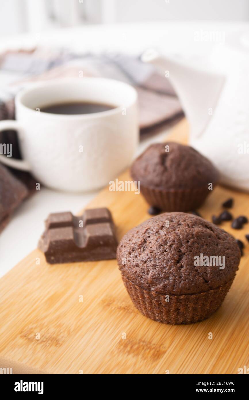 Schokoladenmuffins, Schokoladenchips, Schokoriegel, Tasse Kaffee, Teekanne auf einer Holzfläche mit warmem Schal, Weihnachtsbeleuchtung Bokeh und Stolly in der Stockfoto