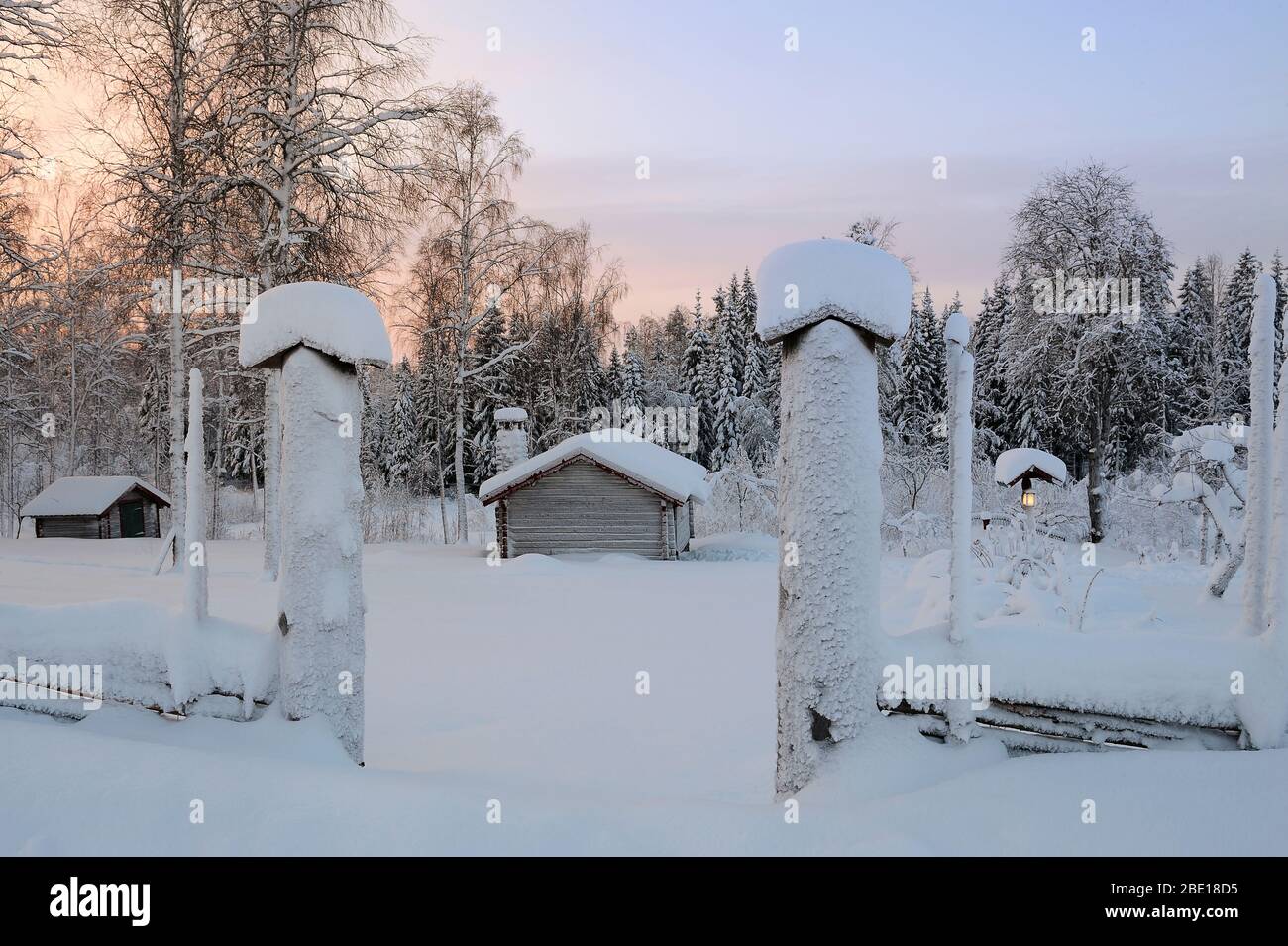 Pfosten und Blockhäuser in einer sonnenbeschwingen Winterlandschaft Stockfoto