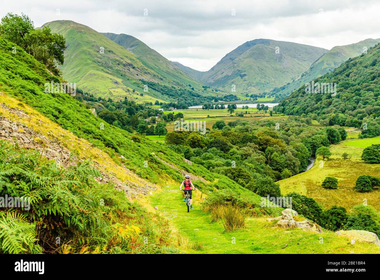 Mountainbiker steigen in Richtung Boredale Hause im Seengebiet. Brothers Water, Caudale Moor, Kirkstone Pass und Red Screes Behind. Stockfoto