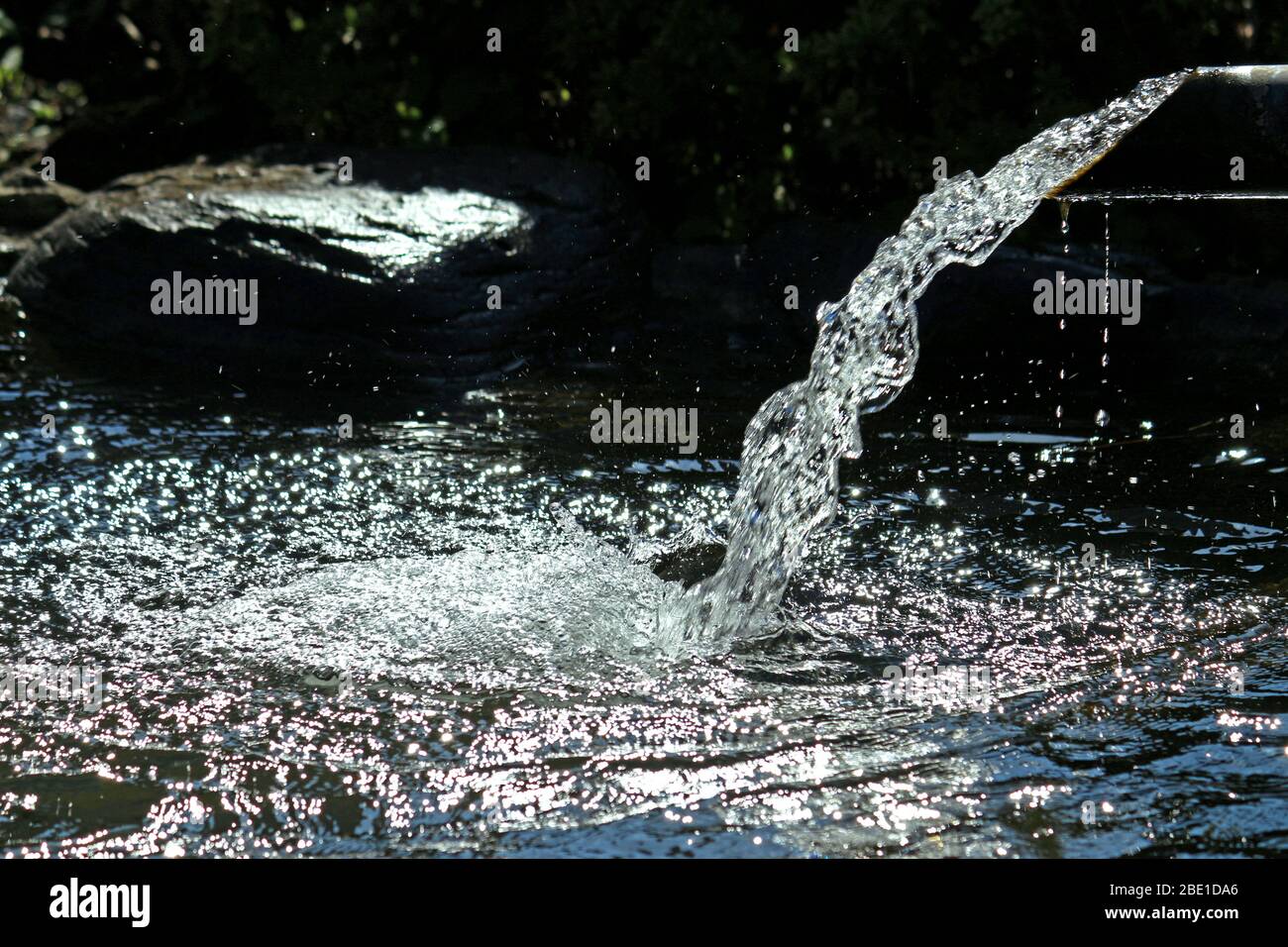 Frisches Wasser fließt aus dem Auslauf in den Gartenteich Stockfoto