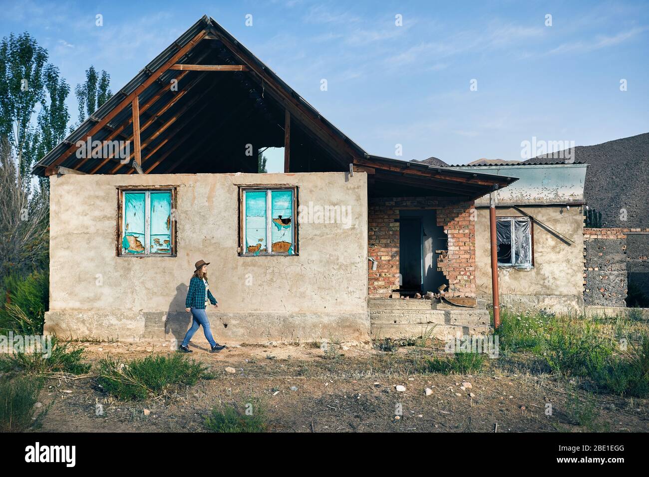 Frau mit Hut und kariertes Hemd zu Fuß in der Nähe von zerstörten alten Haus im Dorf Stockfoto