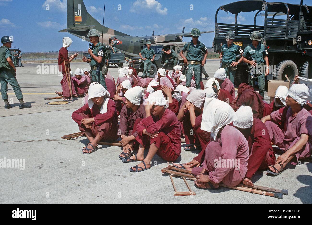 Viet Cong Kriegsgefangenen sitzen auf der Rampe bei Tan Son Nhut Air Base unter den wachsamen Augen der Südvietnamesischen Militärpolizei. Die Kriegsgefangenen wurden auf der Airbase in der 6x6-Lkw im Hintergrund geholt und wird zu Loc Ninh, South Vietnam auf der C-123 Transportflugzeuge für die Gefangenen Austausch zwischen den Vereinigten Staaten und Nord/Süd Vietnam Vietnam/Viet Cong Militär eingeflogen werden. Stockfoto