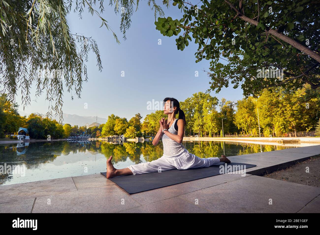 Schöne asiatische Mädchen im weißen Kostüm Yoga in der Nähe der See im Park bei Sonnenaufgang Stockfoto