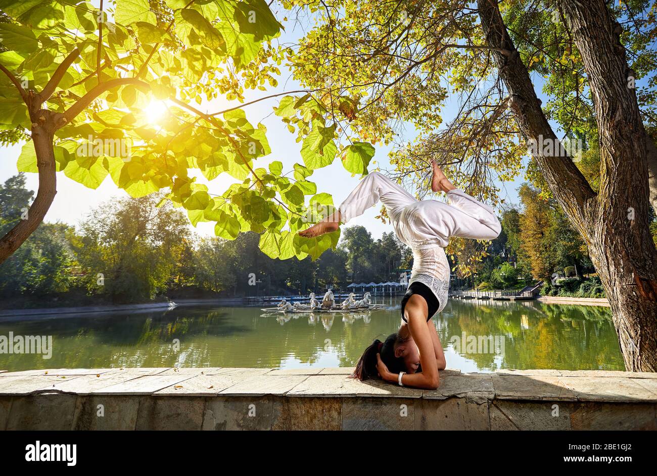 Schöne asiatische Mädchen in weiß Kostüm tun Kopf stehen Yoga-Position im Park Stockfoto