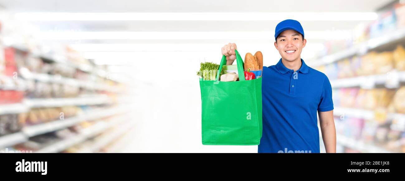 Lächelnd gut aussehend asiatischen Mann hält Lebensmitteleinkaufstasche im Supermarkt Banner Hintergrund mit Kopie spce für Lebensmittel-Lieferservice Konzept Stockfoto