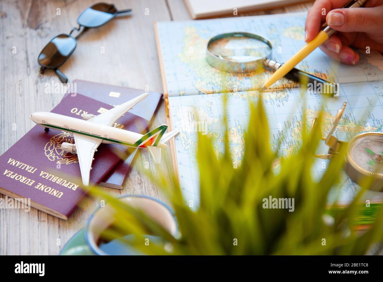 Weibliche Hand hält einen Stift für die Planung Reise mit Weltkarte auf dem Tisch. Reisekonzept. Sonnenbrille, Pässe, Kompass, Spielzeugflugzeug. Das Konzept von Pre Stockfoto