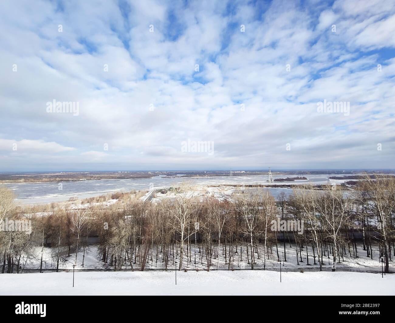 Schöne Flusslandschaft im frühen Frühling. Weiße Wolken über dem Fluss und Bäume an einem sonnigen Tag nach dem Schneeschmelzen. Stockfoto