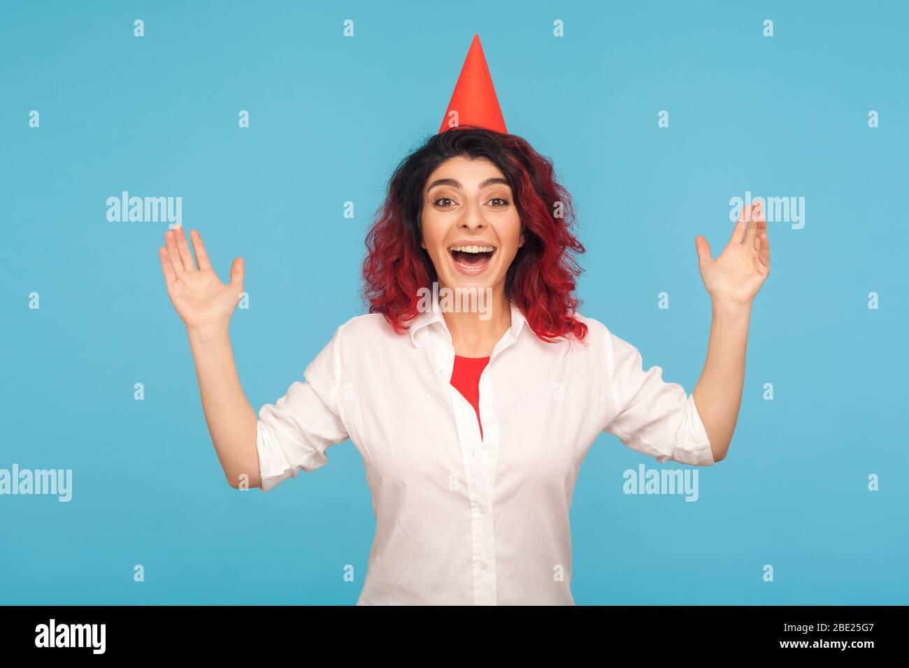 Aufgeregt erstaunt extrem glückliche Frau mit lustigen Party-Kegel auf dem Kopf Heben Hände, schreien freudig mit Bewunderung, emotionale Reaktion auf Geburtstag s Stockfoto