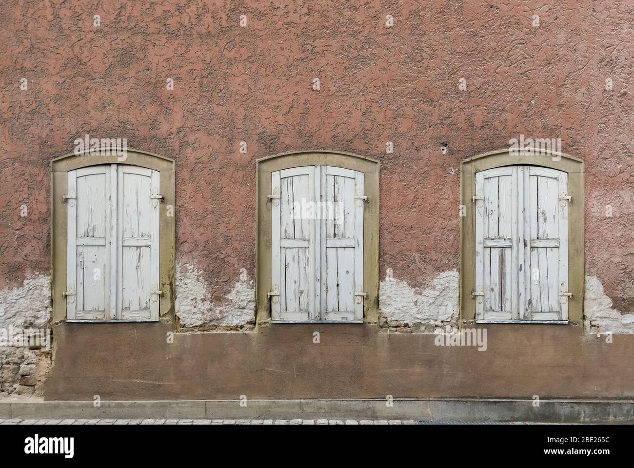 Symmetrische Fassade des verlassenen, baufälligen Hauses mit 3 Fenstern mit Fensterläden Stockfoto