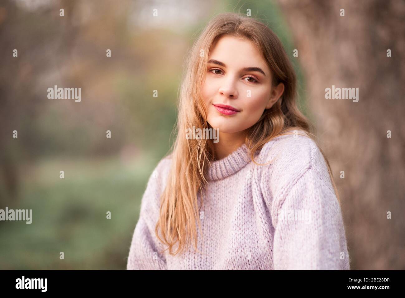 Schöne blonde Teenager-Mädchen 16-18 Jahre alt trägt Strickpullover posiert im Freien über Natur Hintergrund. Betrachten der Kamera. Frühjahrssaison. Stockfoto