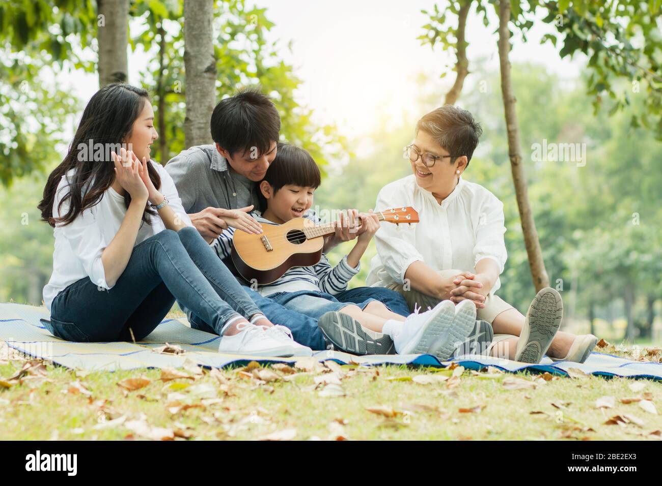 Glückliche Familie mit Oma, Mama mit Papa, der Sohn Gitarre spielt und ein Lied im Park singt, genießen und entspannen Leute Picknick draußen Stockfoto
