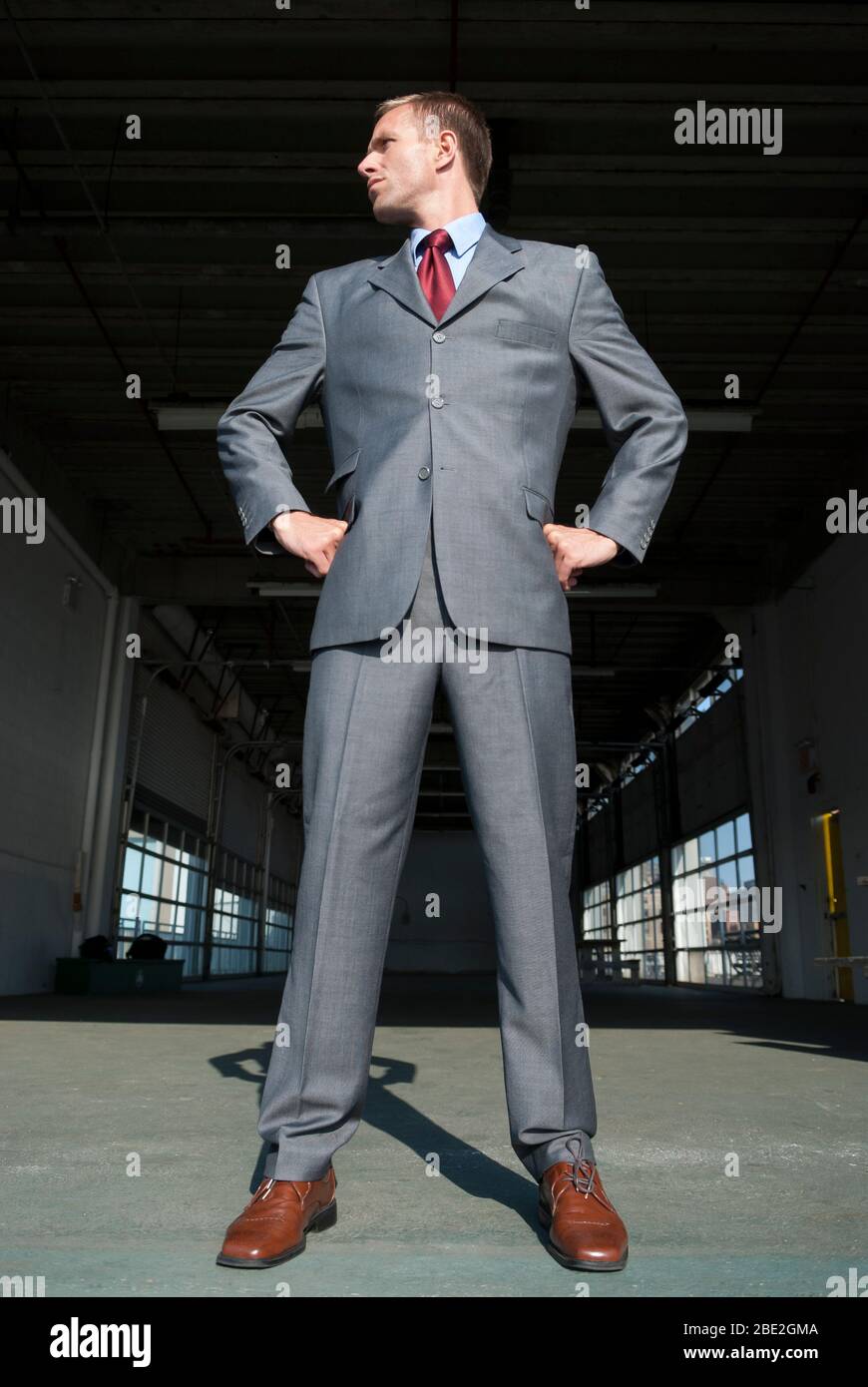 Geschäftsmann in einem glänzenden Anzug hoch im Freien in heller Sonne am Eingang zu einem großen Lager stehen Stockfoto