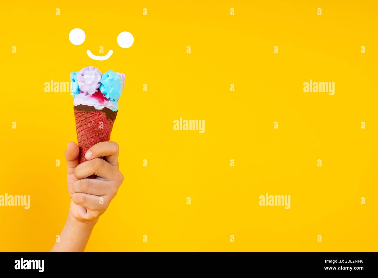 Nahaufnahme Hand hält bunte Eis-Kegel auf gelbem Hintergrund mit Kopierraum Stockfoto