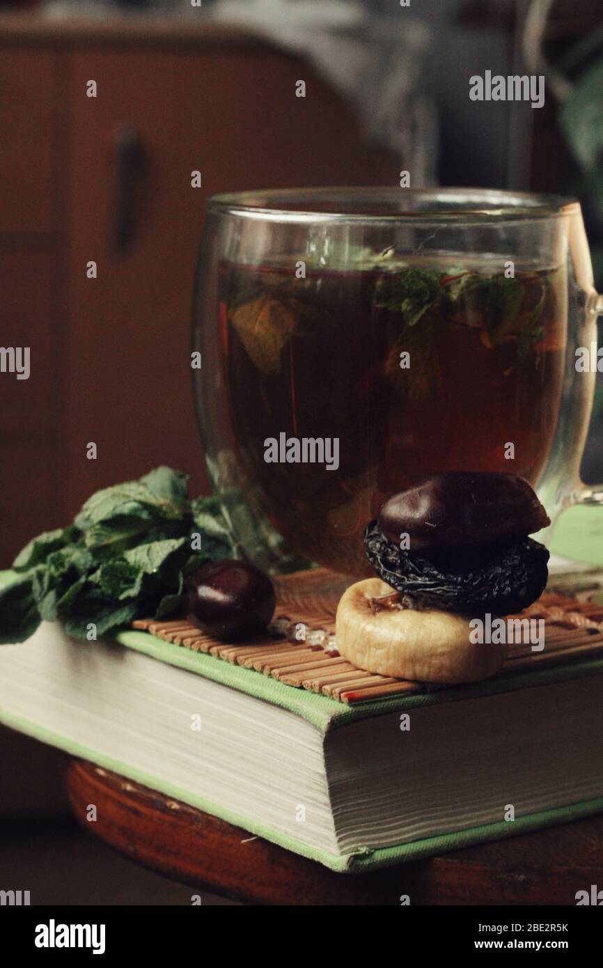 Details. Dunkle mystische und ruhige Stimmung. Buch und heißen Tee mit Minze und Honig auf dem Tisch mit grünen Pflanzen. Frühlingsmorgen zu Hause. Gesundes Getränk. Bildung, Stockfoto