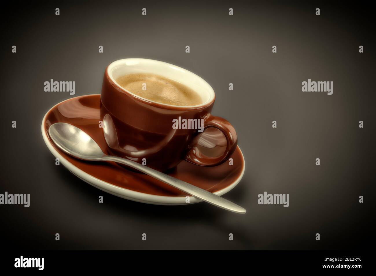 Eine braune kleine Espressotasse mit Loeffel vor schwarzem Hintergrund Stockfoto