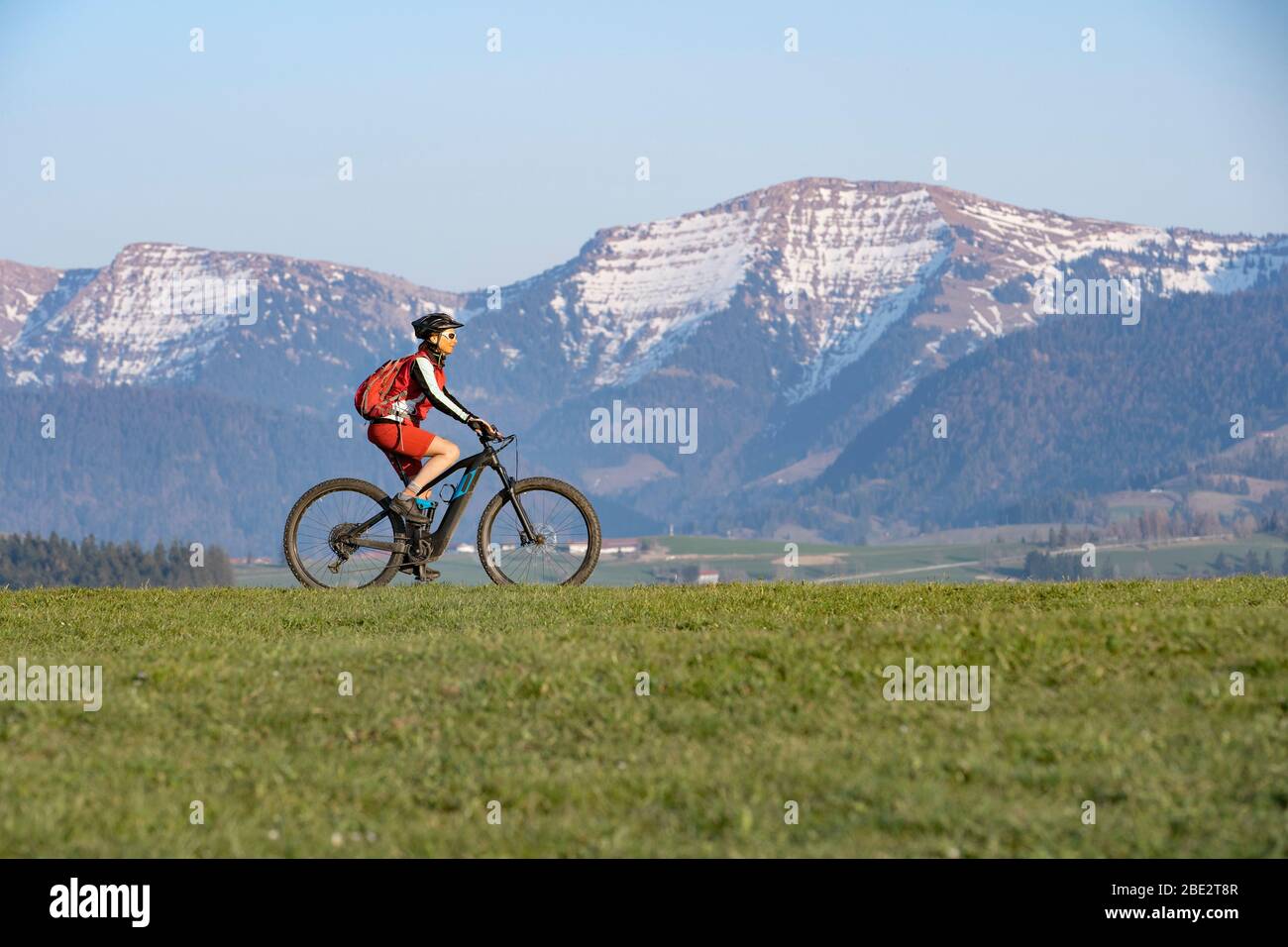 Hübsche ältere Frau, die im Frühfrühling im Allgäu bei Oberstaufen mit dem Elektro-Mountainbike unterwegs ist, im warmen Abendlicht unter dem sp Stockfoto