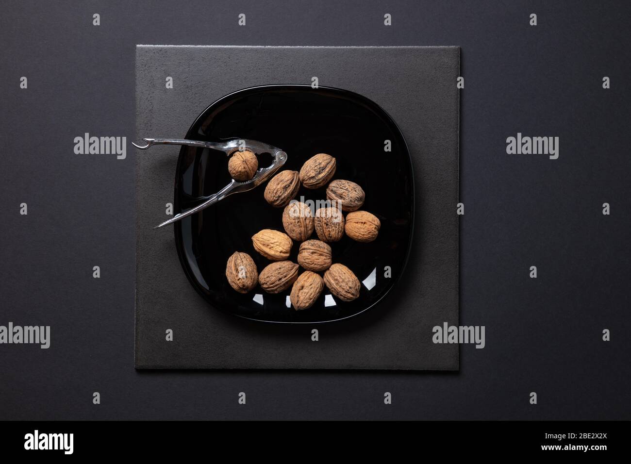 Ein fantastisches Stillleben-Studiobild von Wallnuts auf schwarzem Teller & Nussknacker auf schwarzem dunklen Hintergrund, topview Stockfoto