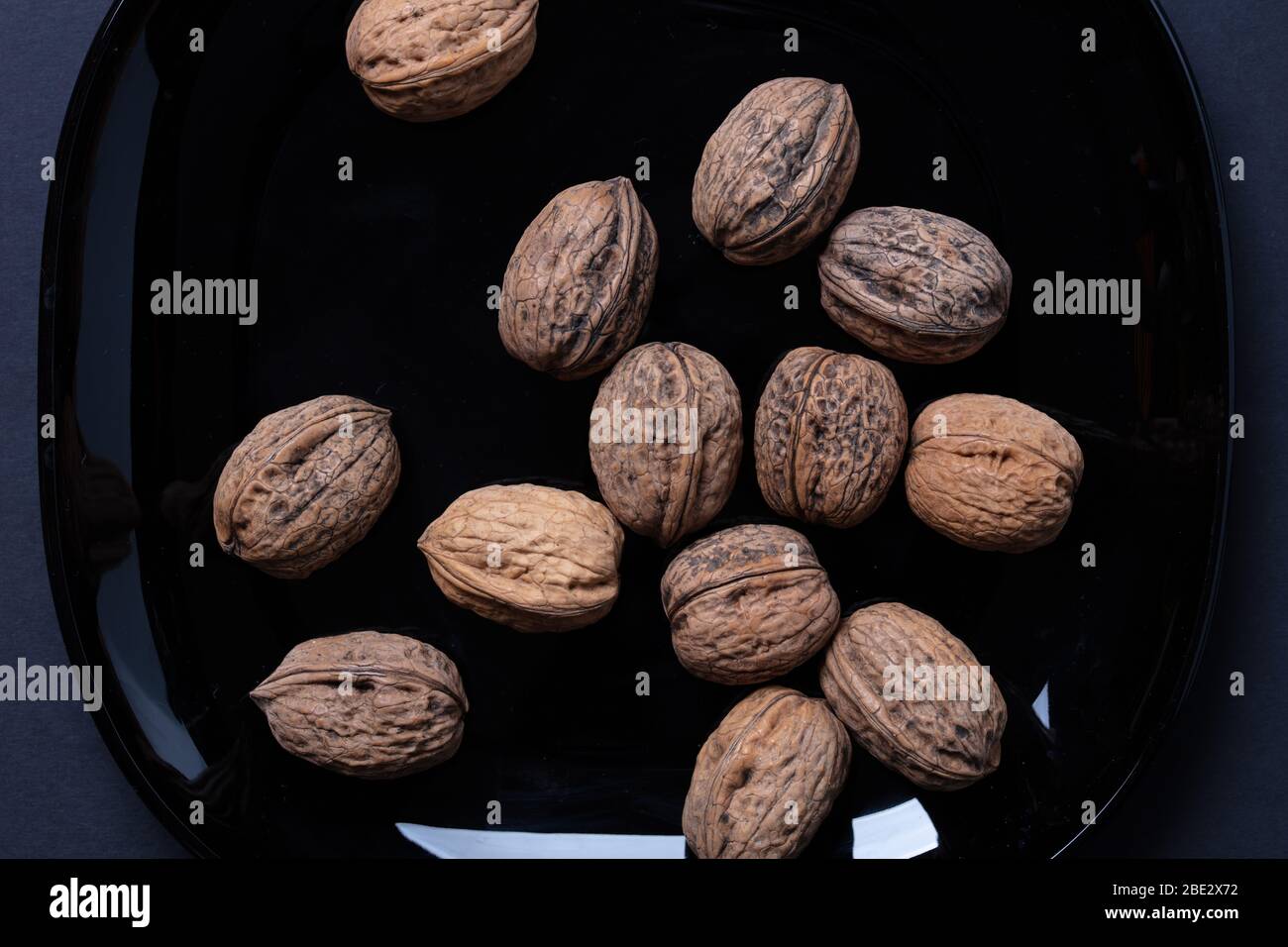 Ein fantastisches Stillleben-Studiobild von Wallnuts auf einer schwarzen Platte auf schwarzem dunklen Hintergrund, topview Stockfoto