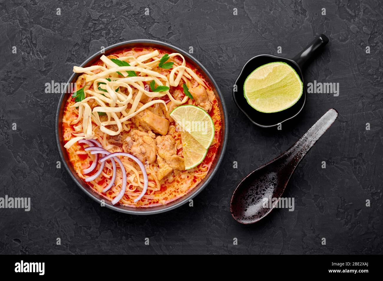 Khao Soi Gai oder Thai Coconut Curry Noodle Suppe in schwarzer Schüssel auf dunklem Schiefergrund. Khao Soy ist Thailand Küche Gericht mit Nudeln, Hühnerfleisch, r Stockfoto
