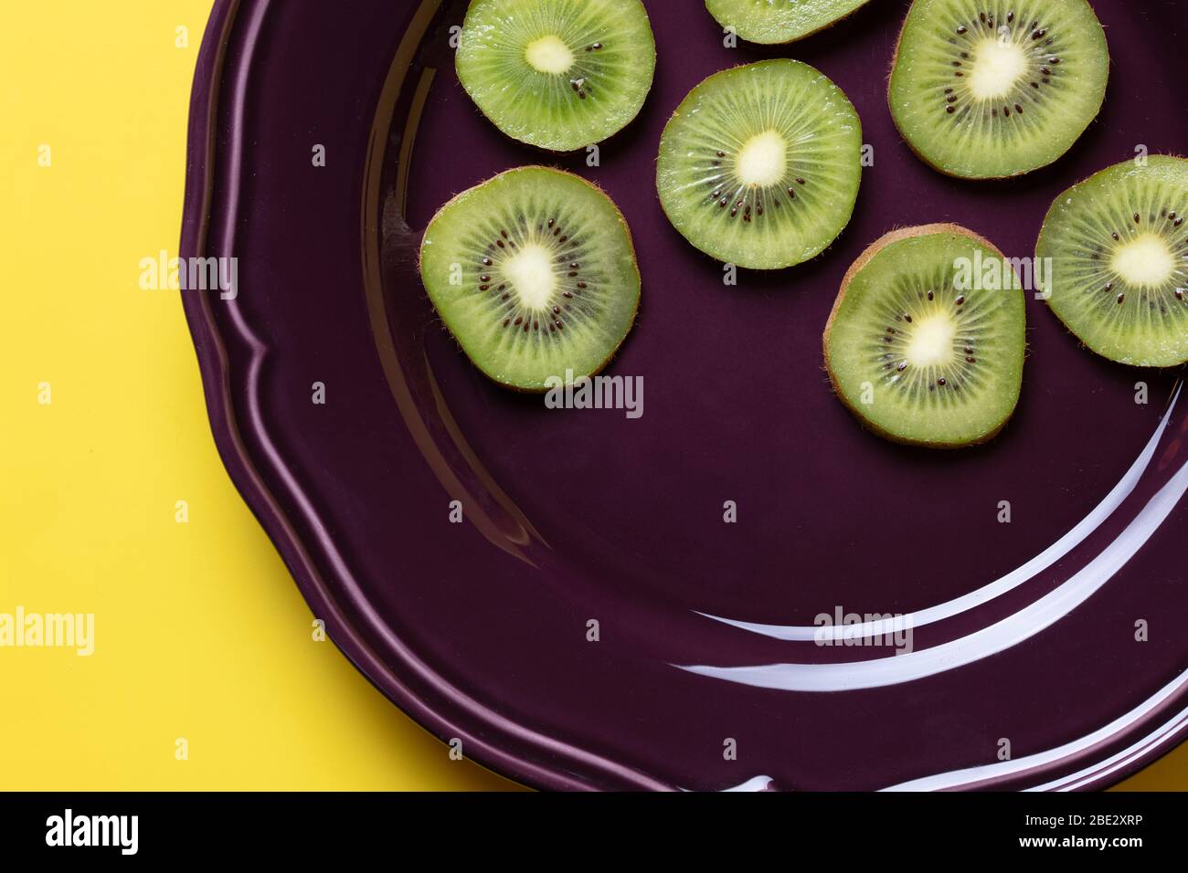 Eine fantastische Stillleben Studio Bildkomposition von frischen leckeren Scheiben Kiwi Früchte auf einem lila Teller und hellgelben Hintergrund, topview Stockfoto