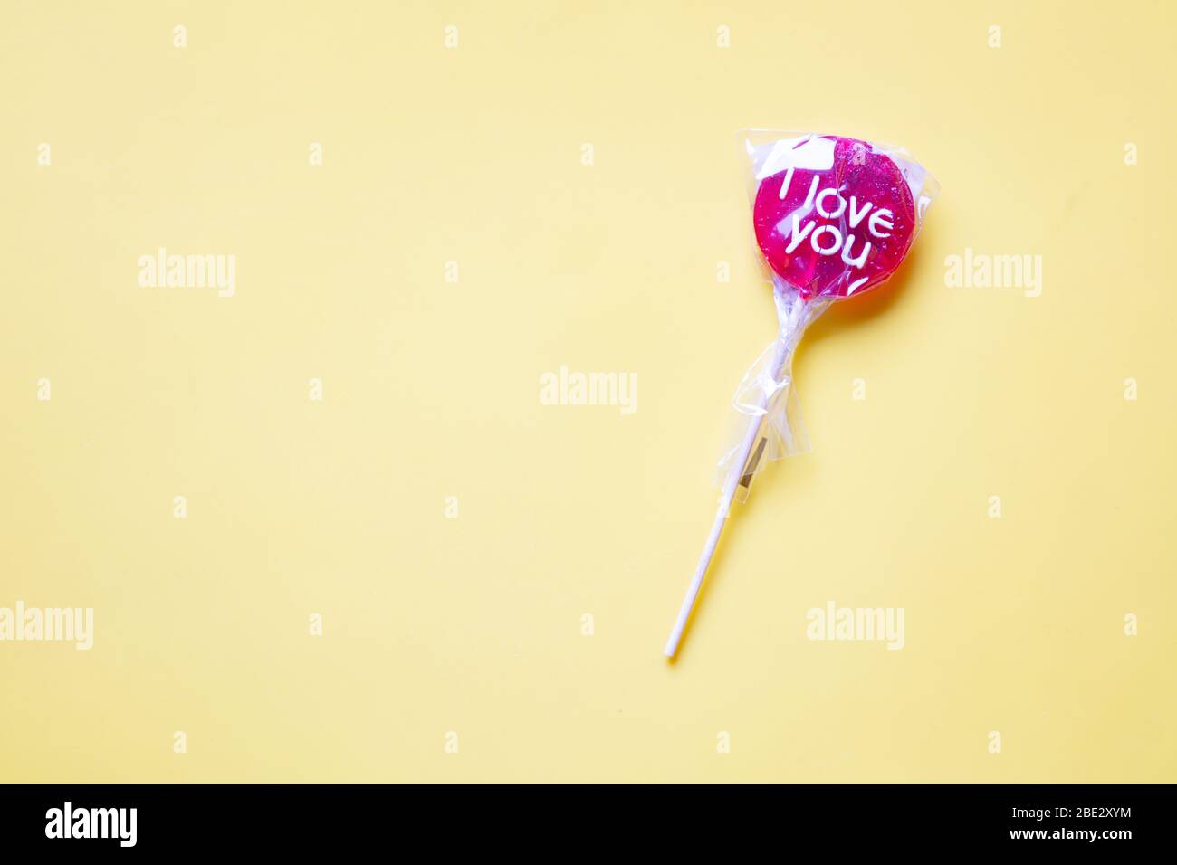 Ein süßes gewickeltes 'I Love You' rotes Lollypop vor einem pastellgelben Hintergrund Stockfoto