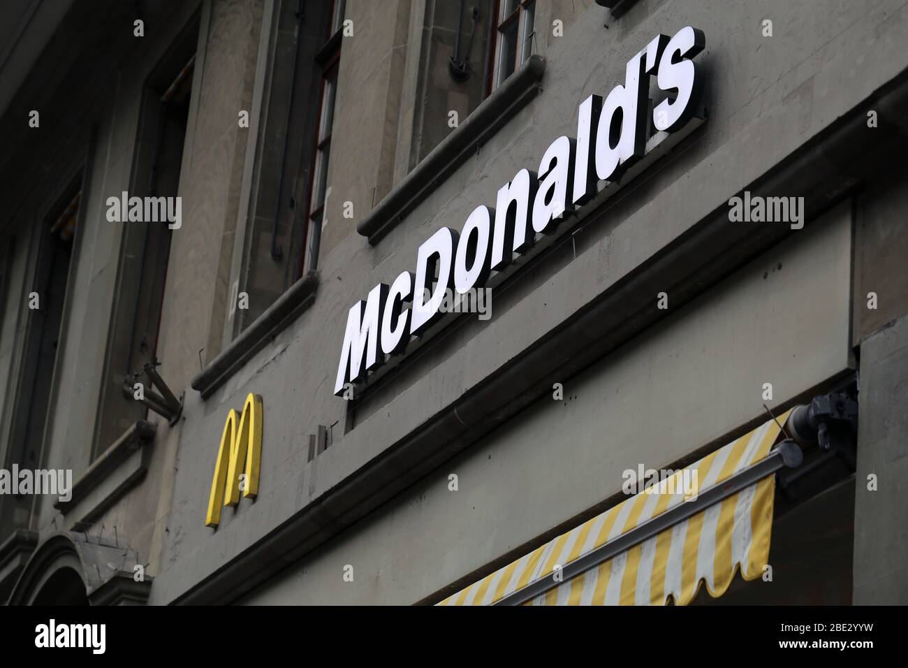 Logo-Schild von McDonald's an der Wand eines alten Gebäudes in der Innenstadt von Bern, Schweiz, März 2020. McDonald's ist eine amerikanische Fast-Food-Kette. Stockfoto