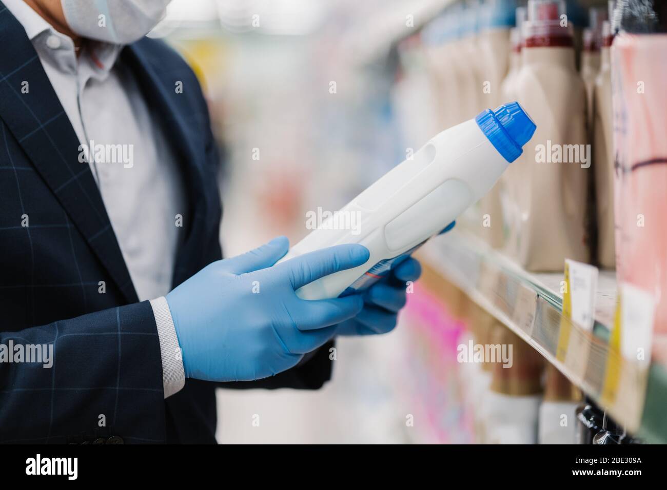 Unbekannter Mann trägt schützende Gummihandschuhe, wählt Haushaltschemikalien, wählt Waschpulver im Geschäft, posiert in der Abteilung Reinigungsprodukt, pro Stockfoto