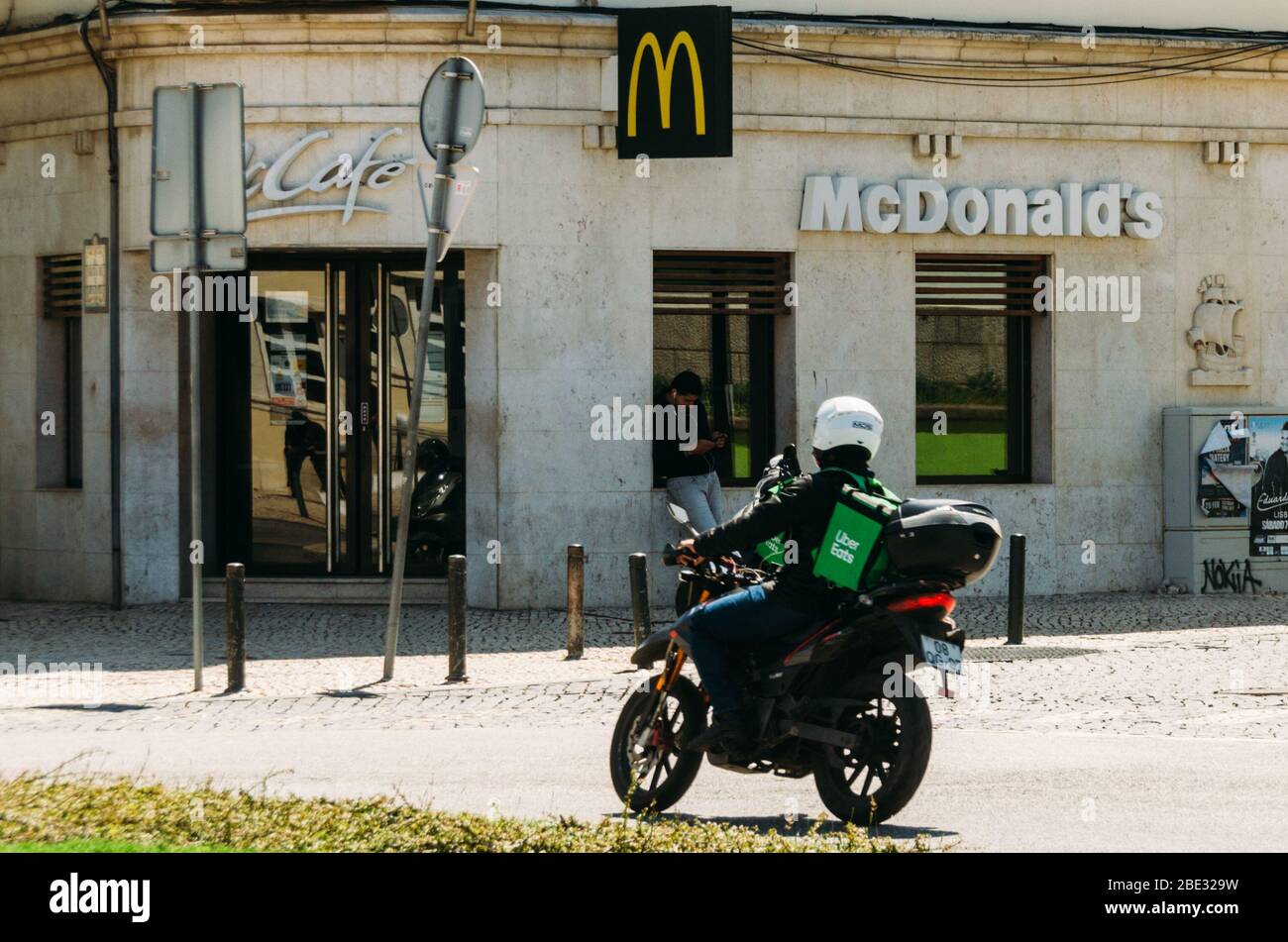 Cascais, Portugal - 11. April 2020: Glovo und UberEats Lieferkuriere auf dem Motorrad vor einem McDonalds Restaurant während des Coronavirus Covid- Stockfoto