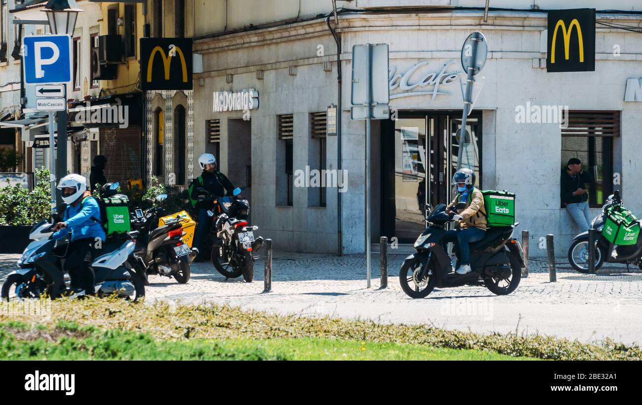 Cascais, Portugal - 11. April 2020: Glovo und UberEats Lieferkuriere auf dem Motorrad vor einem McDonalds Restaurant während des Coronavirus Covid- Stockfoto